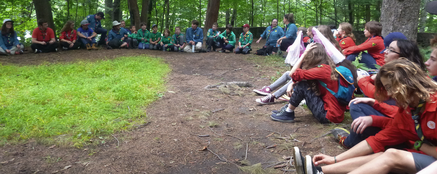 L'image du hero du site des scouts représentant un groupe de scout assis en cercle sur le sol à l'extérieur